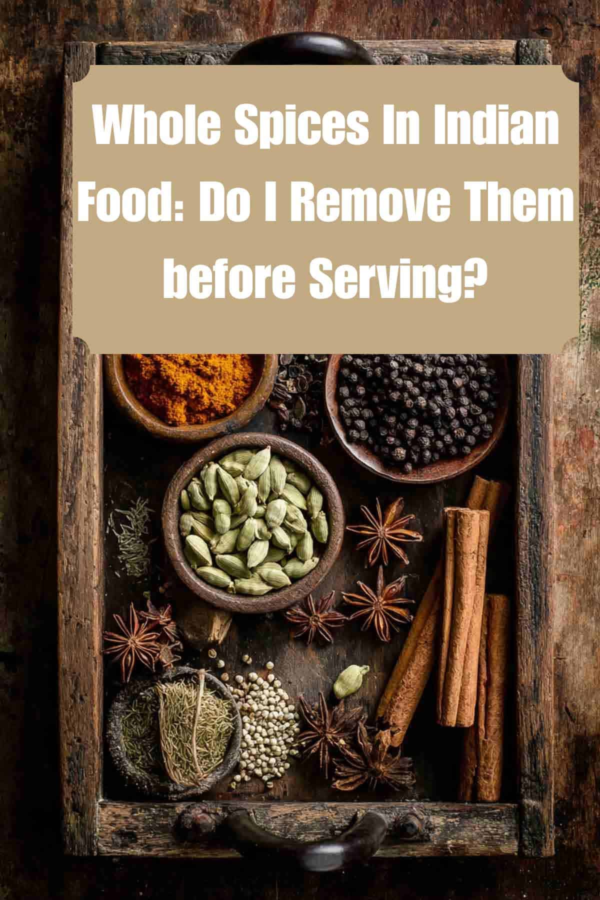 A rustic wooden tray holds bowls of whole spices such as peppercorns, star anise, cinnamon sticks, and more. Text overlay asks if you should remove whole spices before serving Indian food.