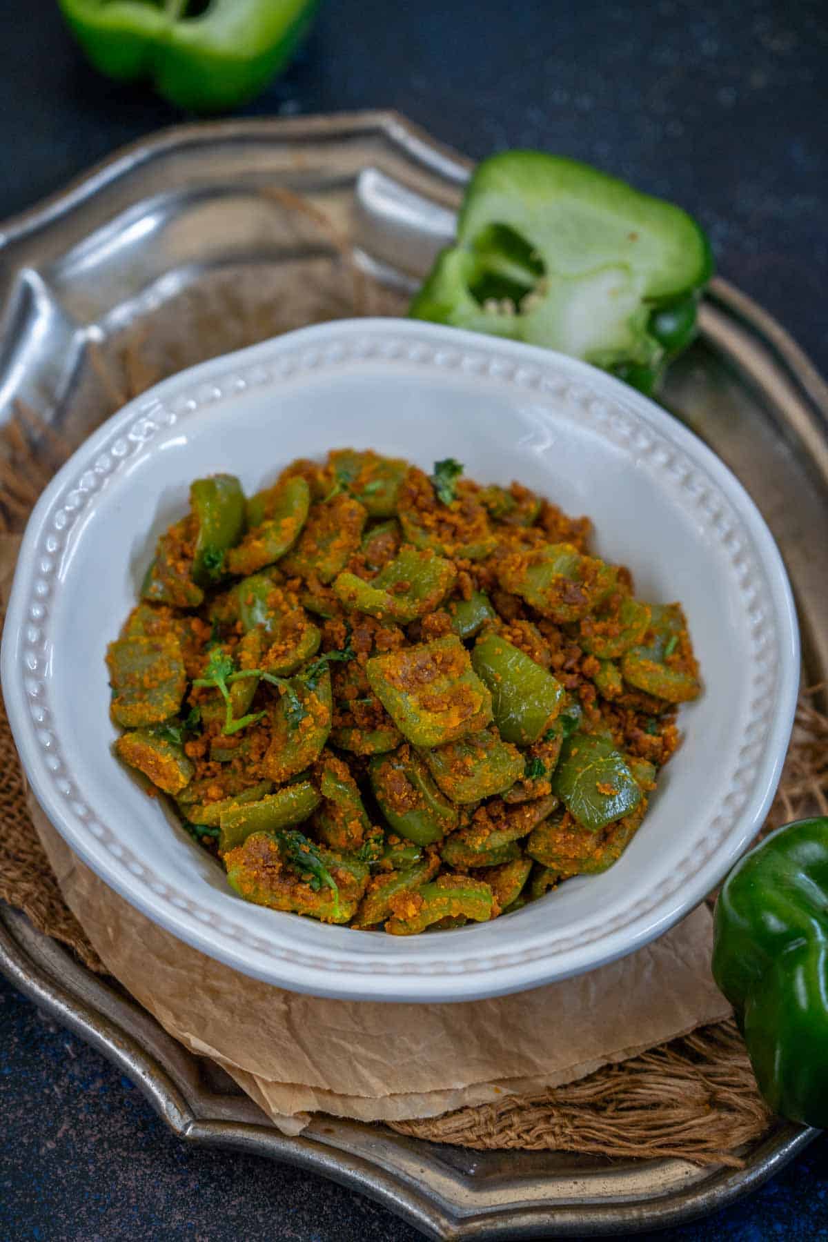A white bowl filled with capsicum besan sabji garnished with fresh cilantro, placed on a rustic surface.