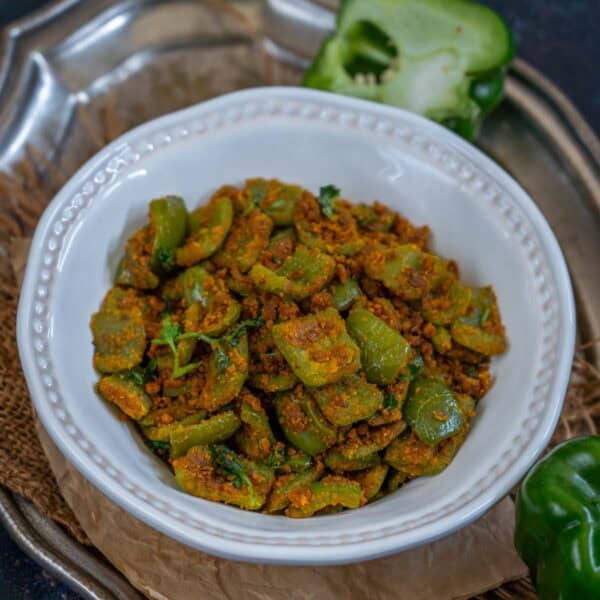 A white bowl filled with capsicum besan sabji garnished with fresh cilantro, placed on a rustic surface.
