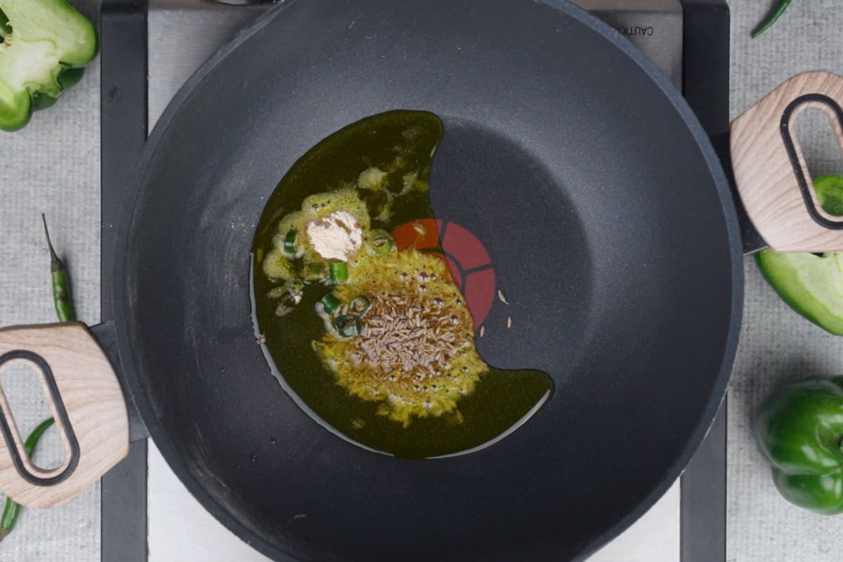 Hing, cumin seeds and green chilies added to hot oil in a pan.