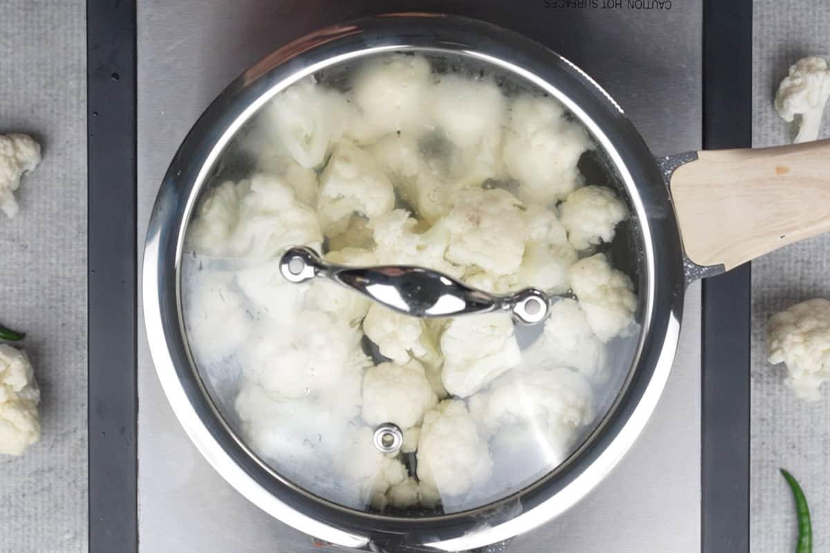 Cauliflower florets cooking in water in a covered pan.