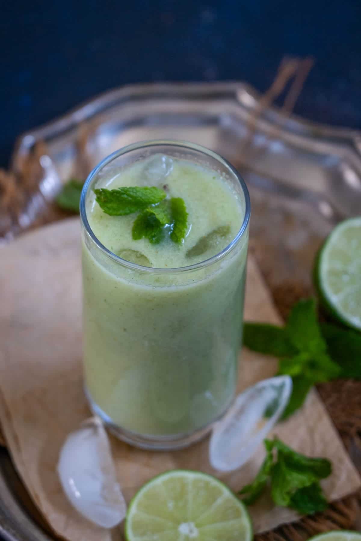 A glass of refreshing lauki juice with ice, garnished with fresh mint leaves, sits on a tray next to a lime half and more mint leaves.