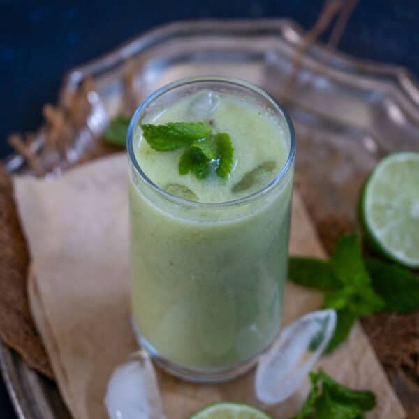 A glass of refreshing lauki juice with ice, garnished with fresh mint leaves, sits on a tray next to a lime half and more mint leaves.