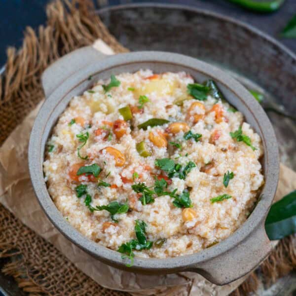 A bowl of samak rice khichdi garnished with chopped cilantro and vegetables, served in a rustic dish on a tray with brown fabric underneath.