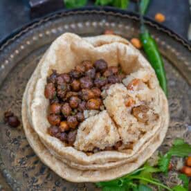 A metal plate with a stack of poori topped with sookha kala chana and a portion of sooji halwa, garnished with green chili and cilantro.
