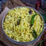 A bowl of cabbage poriyal stir-fry, garnished with mustard seeds, dried red chilies, curry leaves, and a green chili, served on a rustic surface—perfect for anyone searching for an authentic Cabbage Poriyal Recipe.