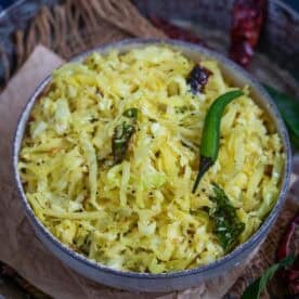 A bowl of cabbage poriyal stir-fry, garnished with mustard seeds, dried red chilies, curry leaves, and a green chili, served on a rustic surface—perfect for anyone searching for an authentic Cabbage Poriyal Recipe.