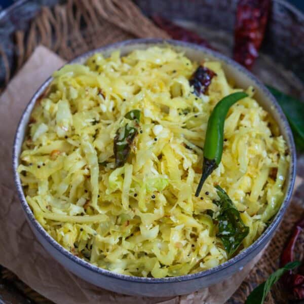 A bowl of cabbage poriyal stir-fry, garnished with mustard seeds, dried red chilies, curry leaves, and a green chili, served on a rustic surface—perfect for anyone searching for an authentic Cabbage Poriyal Recipe.