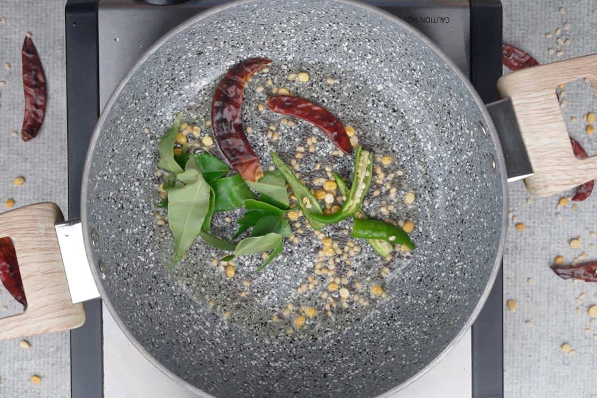 Curry leaves, dried red chilies and green chilies added to the pan.