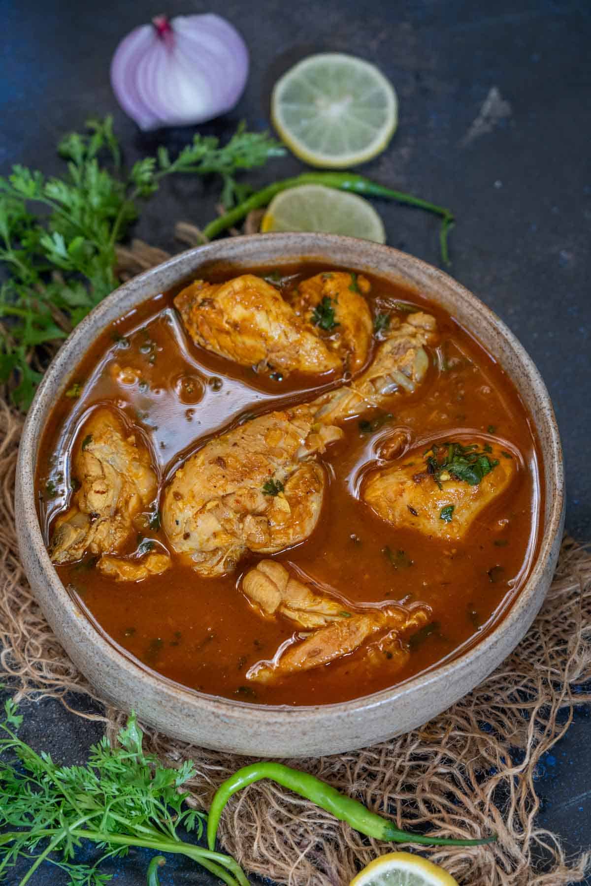 A bowl of Pahadi Chicken Curry with several pieces of chicken in a rich, brown, spiced gravy, garnished with chopped herbs. This authentic Chicken Curry Recipe captures the bold flavors and aromatic spices of traditional Pahadi cuisine.