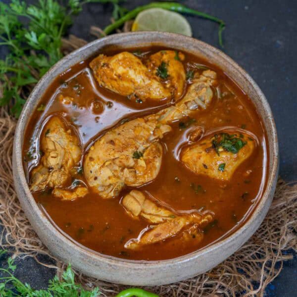 A bowl of Pahadi Chicken Curry with several pieces of chicken in a rich, brown, spiced gravy, garnished with chopped herbs. This authentic Chicken Curry Recipe captures the bold flavors and aromatic spices of traditional Pahadi cuisine.